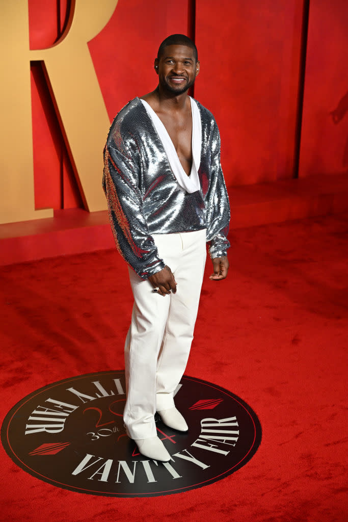 Man in a silver jacket and white pants stands on a red carpet