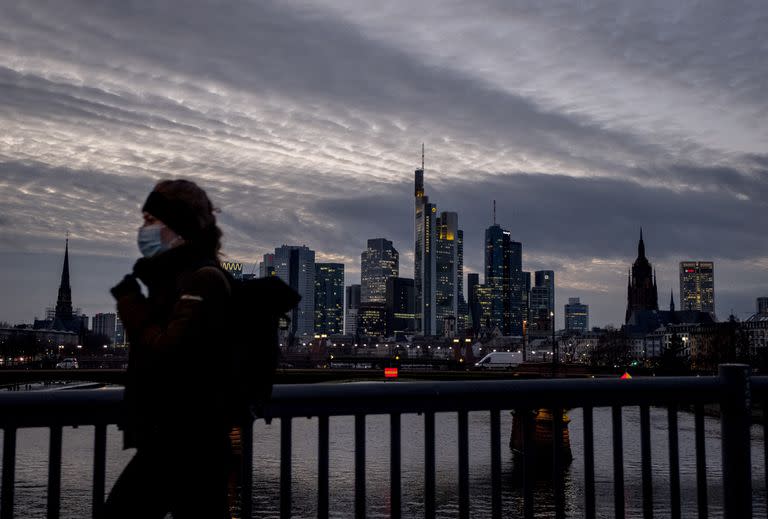 Una mujer con barbijo asa caminando mientras al fondo se observa la ciudad de Fráncfort, Alemania