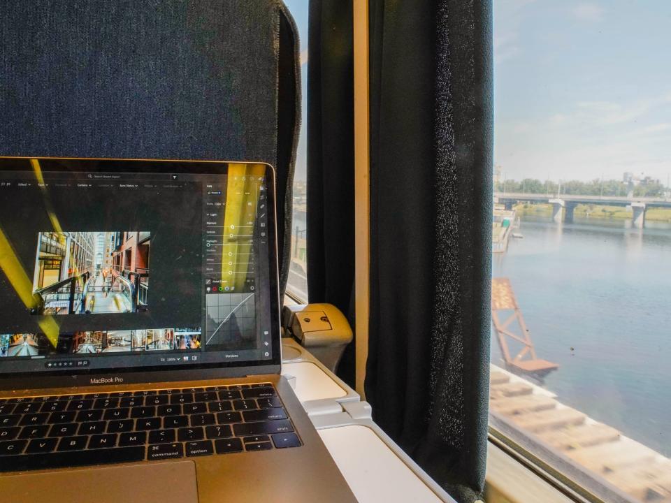 A laptop on a train tray table on the left with a view of water out the window on the right