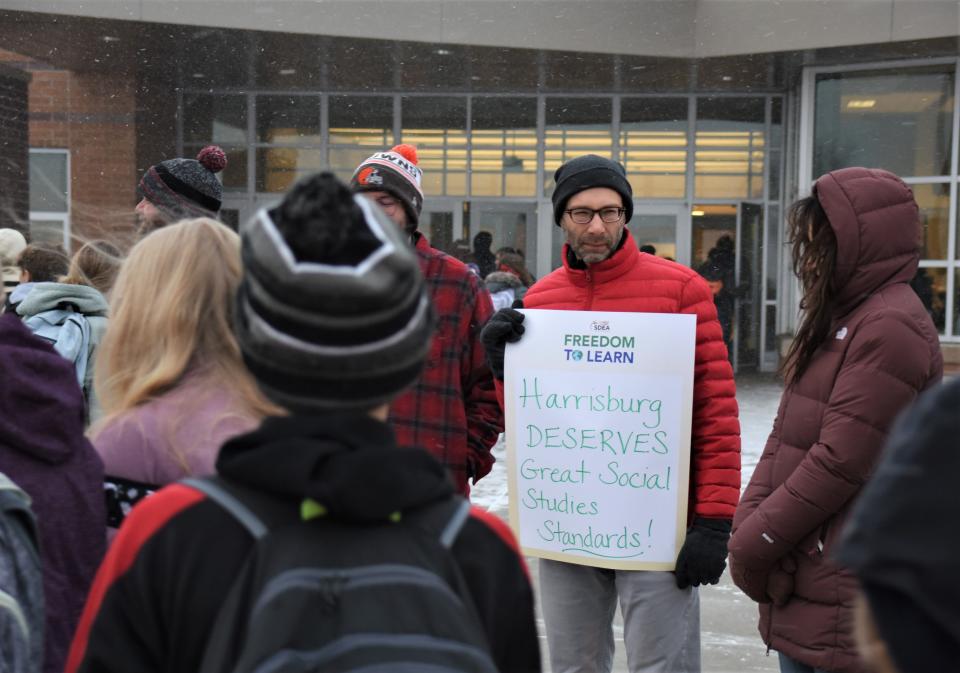 Lyle Kovalenko, a sixth and eighth grade social studies teacher at North Middle School in Harrisburg, holds a sign bearing the message "Harrisburg DESERVES great social studies standards!" as students walk by during a walk-in to school to stand against the proposed social studies standards on Wednesday morning, Nov. 16, 2022.