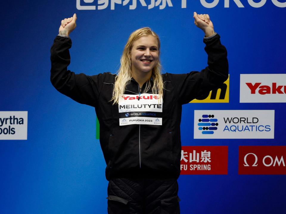 Wearing a black warm-up outfit Lithuania's Ruta Meilutyte celebrates on the podium after winning the women's 50m breastroke final at the Fukuoka 2023 World Aquatics Championships