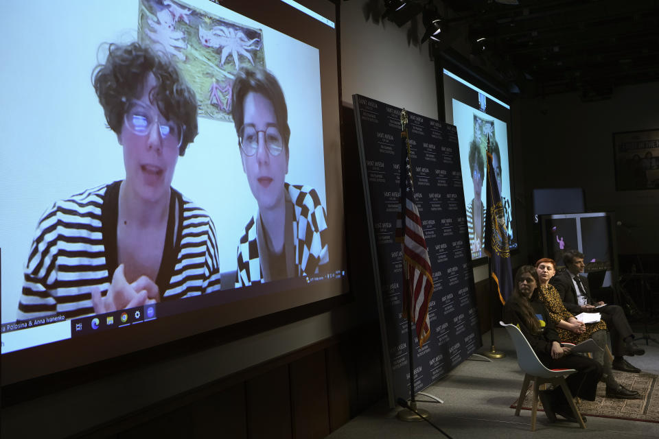 Jenya Polosina, left, and Anna Ivanenko, second from left, both Kyiv, Ukraine-based artists, appear from Kyiv via video link on a screen at art opening for an exhibit called "Our Fire is Stronger Than Your Bombs" at Saint Anselm College in Manchester, N.H., Monday, May 1, 2023. The art exhibit marking the one-year anniversary of the Russian invasion of Ukraine features new work by Ukrainian illustrators some of whom have been living without electricity or water. (AP Photo/Steven Senne)