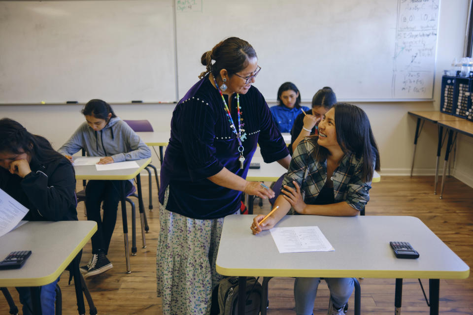 A high school teacher with a group of students in a school classroom.