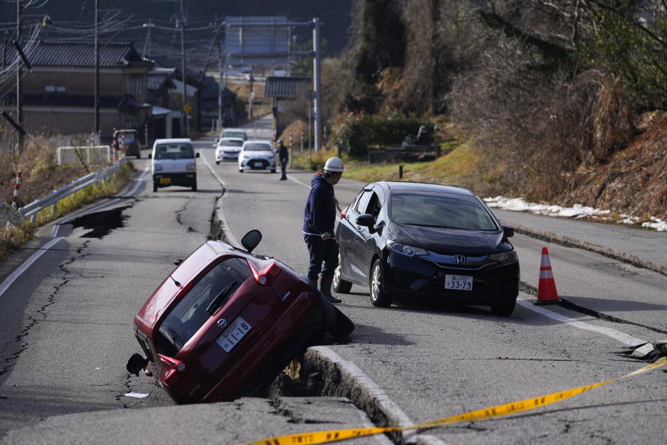 A man directs a driver moving through a damaged street near Anamizu town in the Noto peninsula facing the Sea of Japan, northwest of Tokyo, Tuesday, Jan. 2, 2024, following Monday's deadly earthquake. A series of powerful earthquakes that hit western Japan damaged thousands of buildings, vehicles and boats. Officials warned that more quakes could lie ahead. (AP Photo/Hiro Komae)