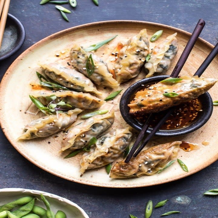 A plate of crispy vegetable potstickers surrounding a small owl of dipping sauce