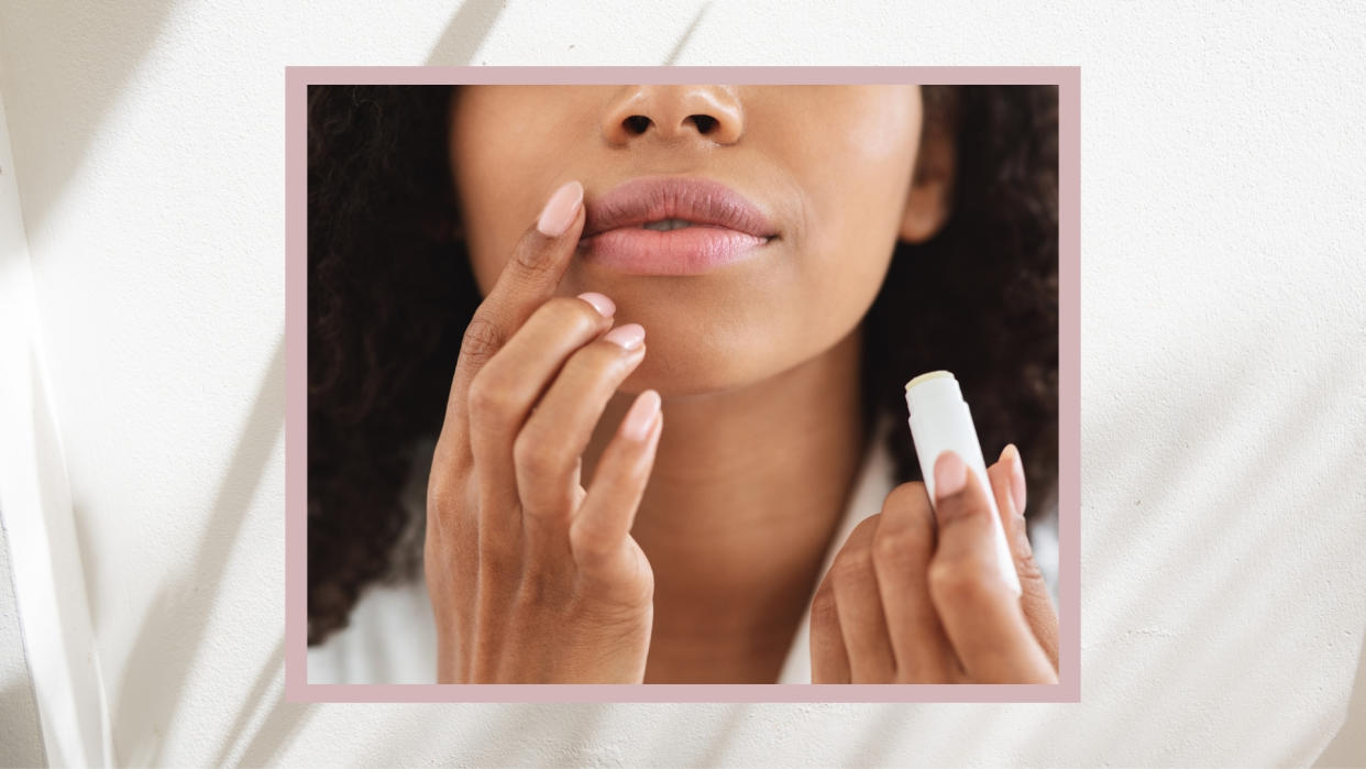  A close up of a woman holding a lip balm and applying it to her lips with her finger/ in a pink and cream template. 