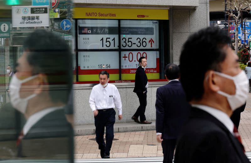 FILE PHOTO: Pedestrians walk past an electric monitor displaying the Japanese yen exchange rate against the U.S. dollar outside a brokerage in Tokyo
