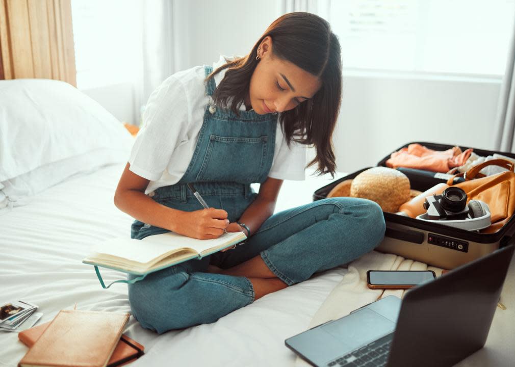 Woman in bedroom with suitcase writing in notebook.