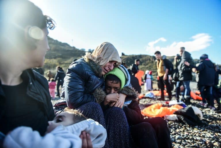 Women and children react as they sit on shore after arriving on the Greek island of Lesbos by crossing the Aegean Sea from Turkey on November 26, 2015