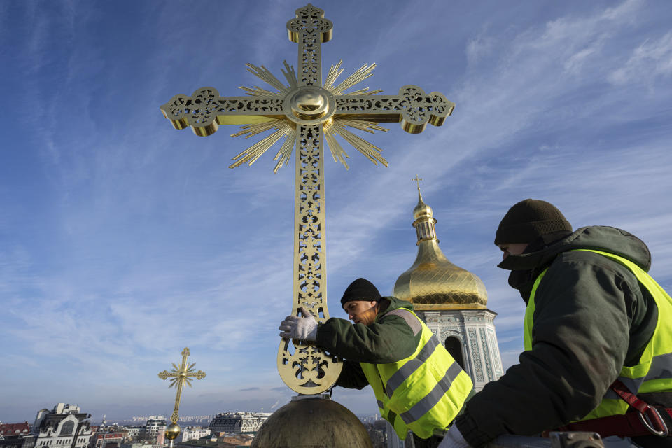 Ihor Kuzmenko, left, and Yuriy Maliuh altitude workers install a restored cross on a dome of Saint Sophia Cathedral in Kyiv, Ukraine, Thursday, Dec. 21, 2023. A UNESCO World Heritage site, the gold-domed St. Sophia Cathedral, located in the heart of Kyiv, was built in the 11th century and designed to rival the Hagia Sophia in Istanbul. The monument to Byzantine art contains the biggest collection of mosaics and frescoes from that period, and is surrounded by monastic buildings dating back to the 17th century. (AP Photo/Evgeniy Maloletka)