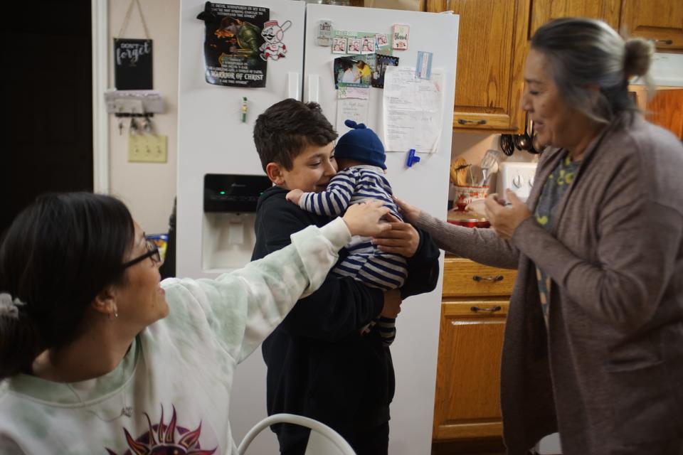 Two women extend their hands to a teen who's holding a baby.
