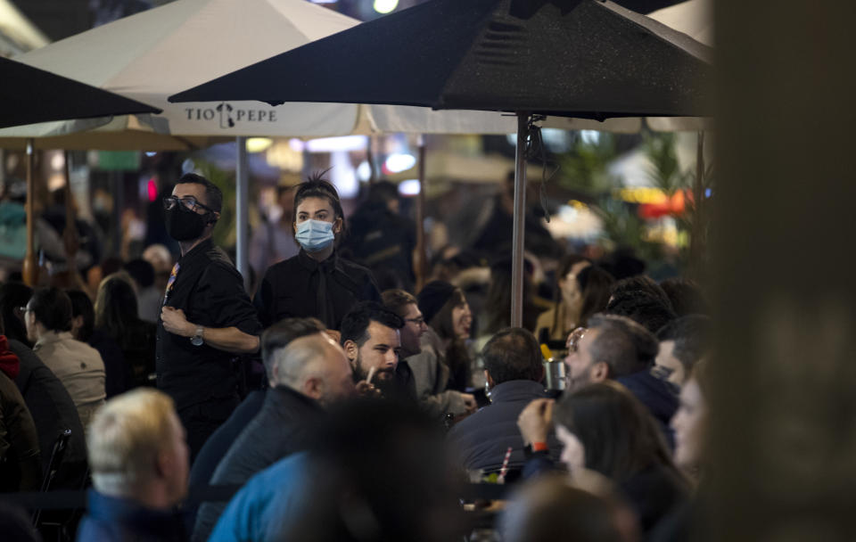 FILE - In this Friday, Oct. 23, 2020 file photo a waiter and waitress wearing masks serve their customers in the pedestrianized part of Old Compton Street in London. (AP Photo/Alastair Grant)