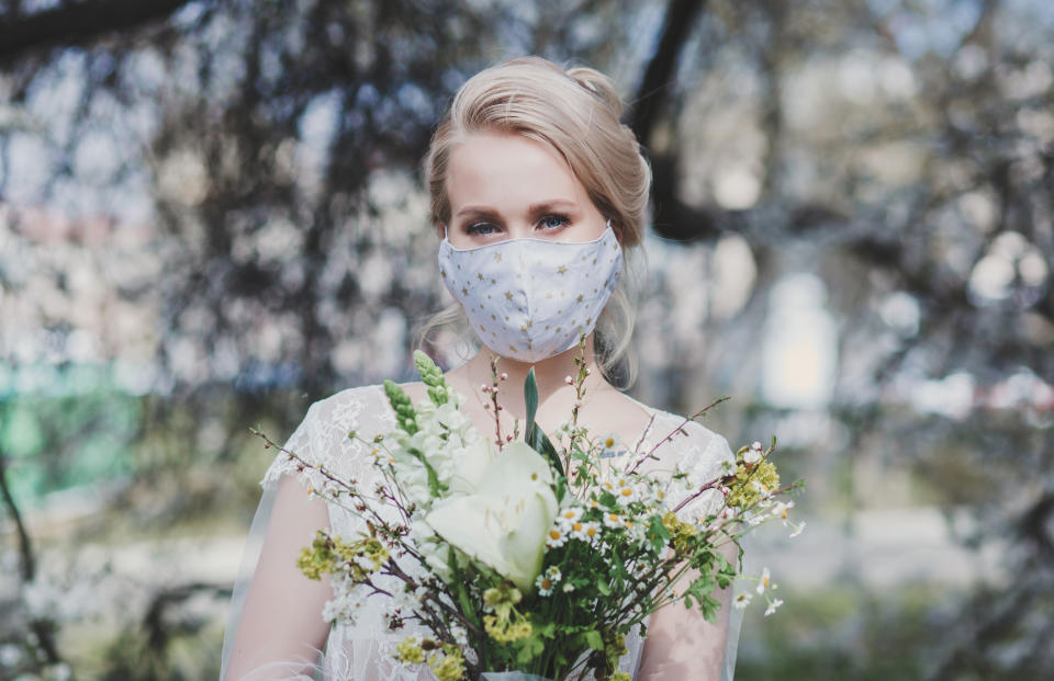 beautiful bride with a bouquet in a protective mask on the background of flowering trees. spring