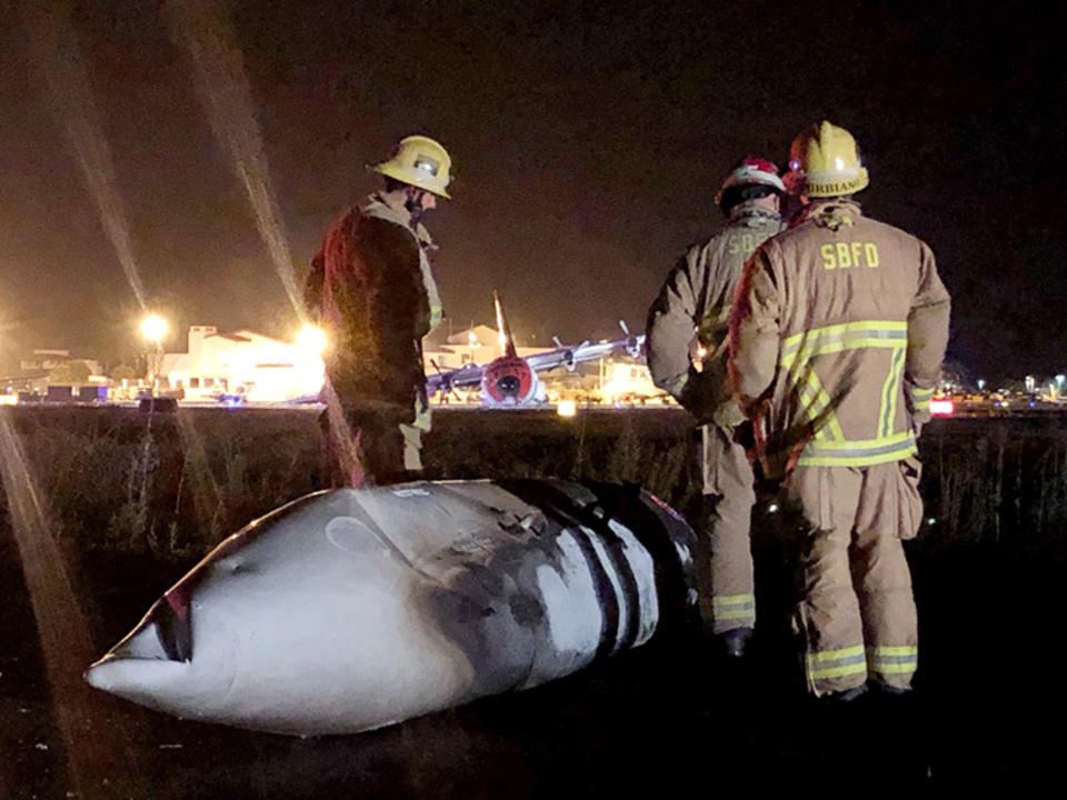 This Sunday, Aug. 25, 2019 photo provided by the Santa Barbara County Fire Department shows the wreckage of a Lockheed C-130 cargo pane after it crashed and burned at the Santa Barbara, Calif., Airport. Authorities say seven people escaped unhurt. The Federal Aviation Administration says the plane experienced hydraulic problems and crash-landed on its belly along a runway. (Mike Eliason/Santa Barbara County Fire Department via AP)