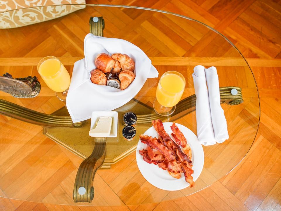 The author's breakfast at the versace mansion with bread, bacon, and orange juice on a glass table