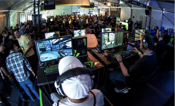 A crowd watches a group of gamers play a video game on PC.