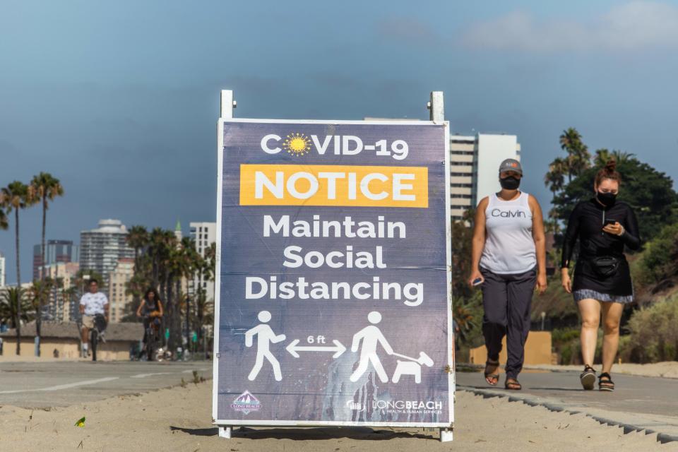 Women wearing facemasks walk near a notice about maintaining social distance on the beach in Long Beach, California, on July 14, 2020. - California's Governor Gavin Newsom announced a significant rollback of the state's reopening plan on July 13, 2020 as coronavirus cases soared across America's richest and most populous state. (Photo by Apu GOMES / AFP) (Photo by APU GOMES/AFP via Getty Images)