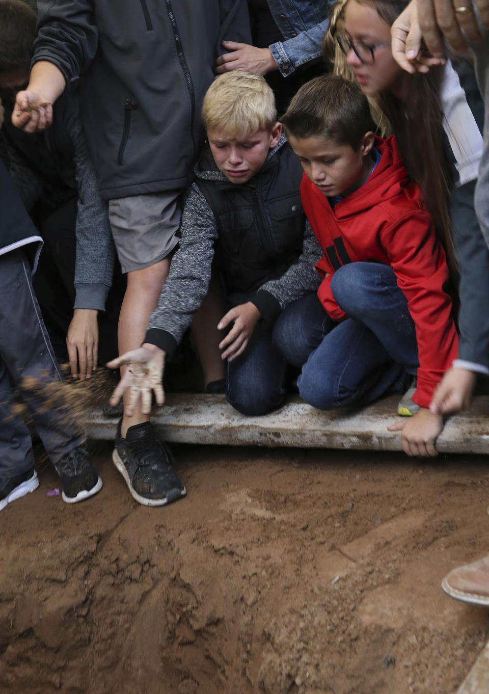 A child tosses a handful of dirt on the coffin that contains the remains of 12-year-old Howard Jacob Miller Jr., at the cemetery in Colonia Le Baron, Mexico, Friday, Nov. 8, 2019, during a burial service for Rhonita Miller and four of her young children. The bodies of Miller and four of her children were taken in a convoy of pickup trucks and SUVS, on the same dirt-and-rock mountainous road where they were killed Monday by drug cartel men, for burial in the community of Colonia Le Baron in Chihuahua state. (AP Photo/Marco Ugarte)