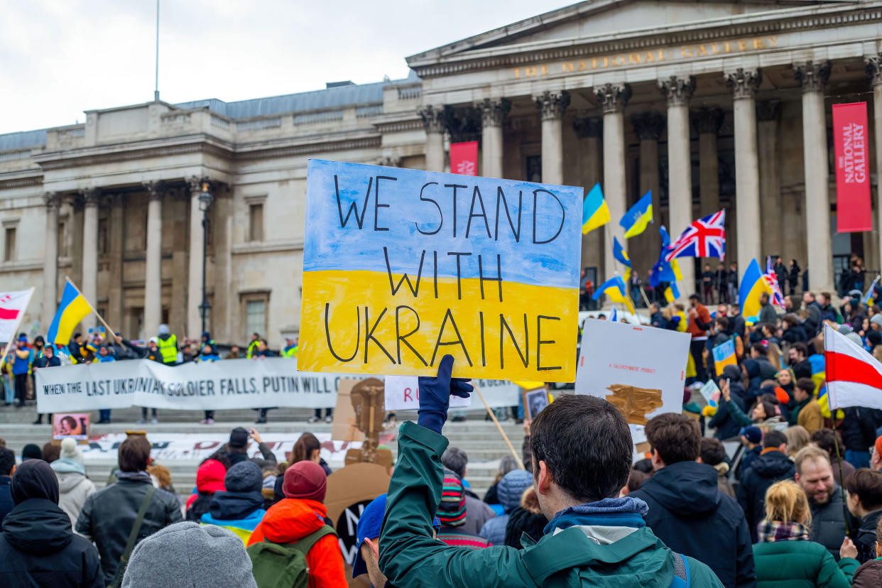 A protester holds a sign saying  "We Stand With Ukraine"