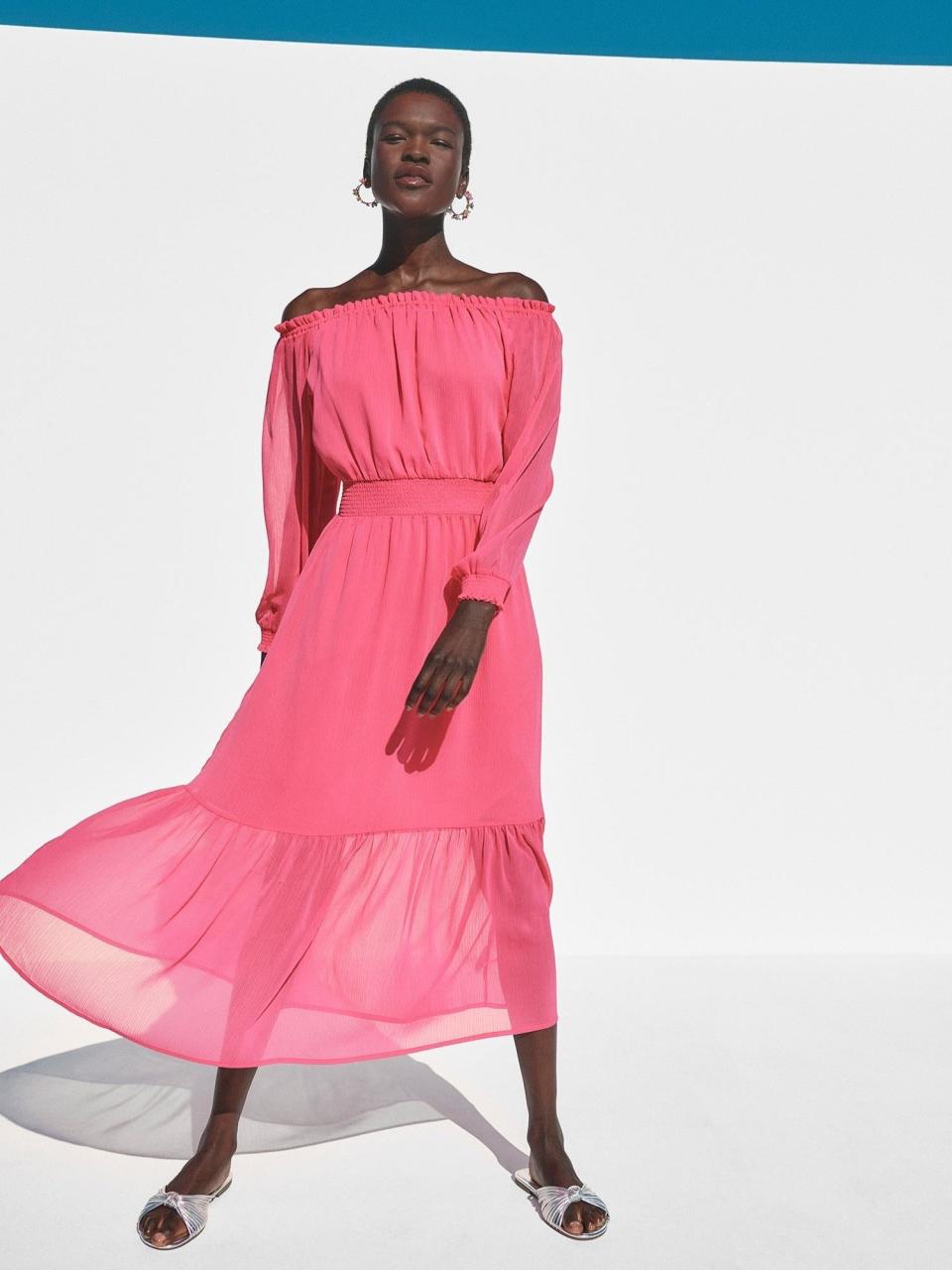 Model in an off-shoulder pink dress with a cinched waist, standing against a two-tone backdrop