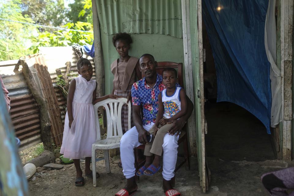 Guens Moliere poses for a photo with his children outside their home in the La Punta community of Santo Domingo, Dominican Republic, Sunday, Nov. 21, 2021. These days, many Haitian migrants and those of Haitian descent stay home out of fear of the authorities, or leave the house one at a time to avoid abandoning a child if both parents are deported. (AP Photo/Matias Delacroix)