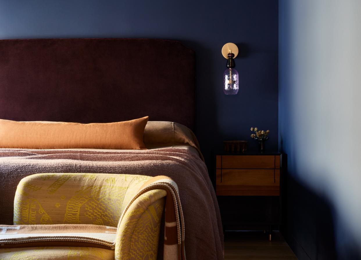  A small bedroom painted dark blue with a gold wall sconce above a wooden nightstand. 