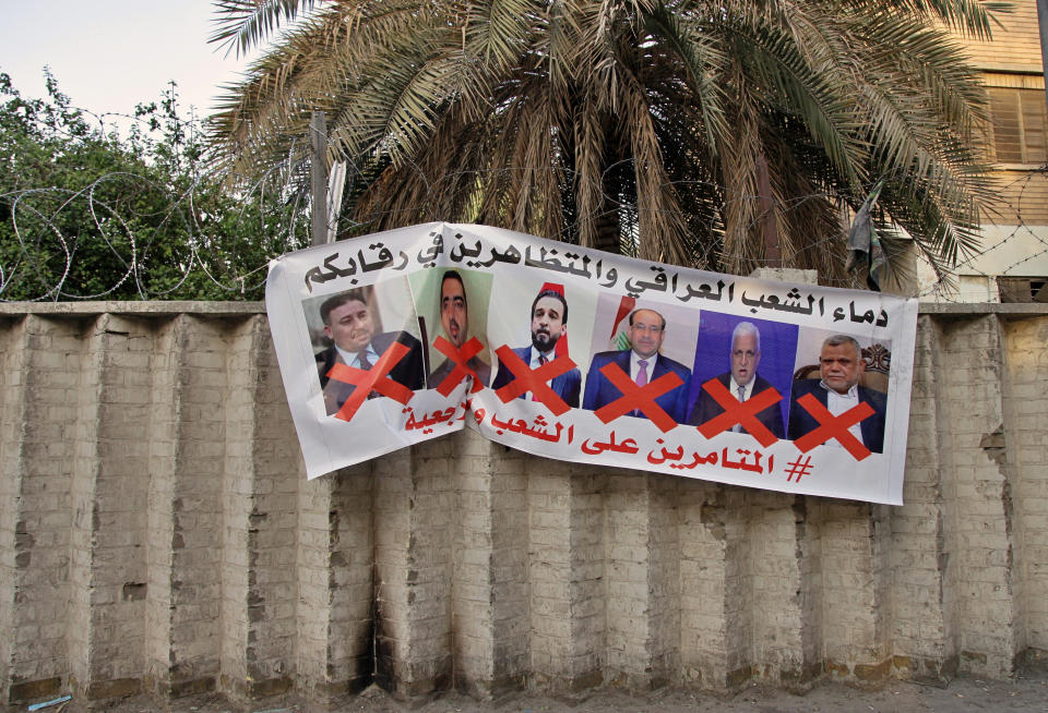 A poster with defaced pictures of Iraqi politicians and Arabic that reads, "the blood of the protesters and the Iraqi people is on your necks, the conspirators on the people and the religious authority," in hung on the wall near Tahrir Square during anti-government demonstrations in Baghdad, Iraq, Thursday, Dec. 26, 2019. (AP Photo/Khalid Mohammed)