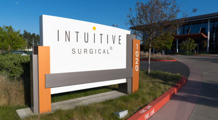 An image of a white, grey, and orange sign with the "Intuitive Surgical" logo and number "1020" on a patch of grass in front of a white, grey, and orange building on a sunny day.