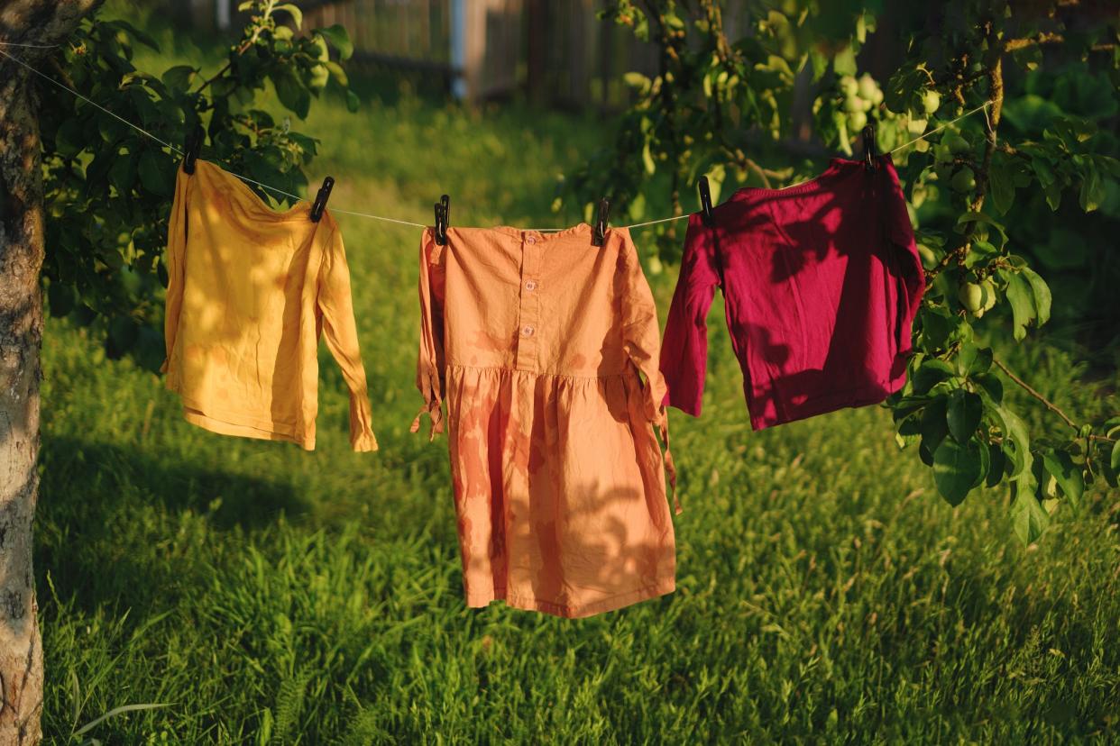 Children's colored clothes dry on clothesline in the garden in nature under rays of the sun after laundering . Protection against fading of colored fabrics. Organic baby washing powders and detergents