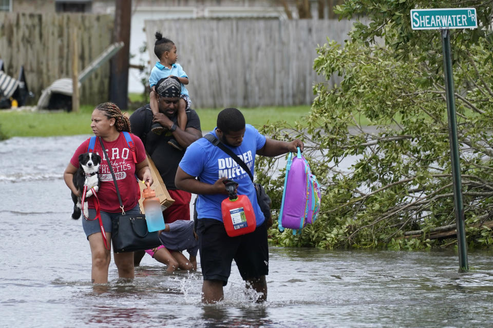 Michael Thomas, back, carries his daughter Mikala, out of his flooded neighborhood after Hurricane Ida moved through Monday, Aug. 30, 2021, in LaPlace, La. (AP Photo/Steve Helber)