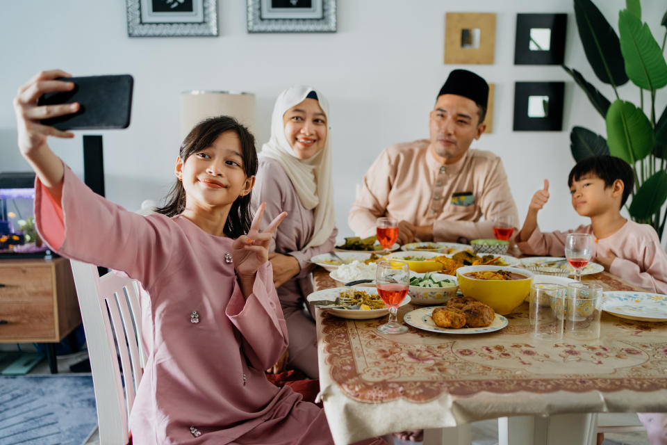 Image of a young Malay girl family taking selfie photo with smartphone during Hari Raya family reunion dinner at home