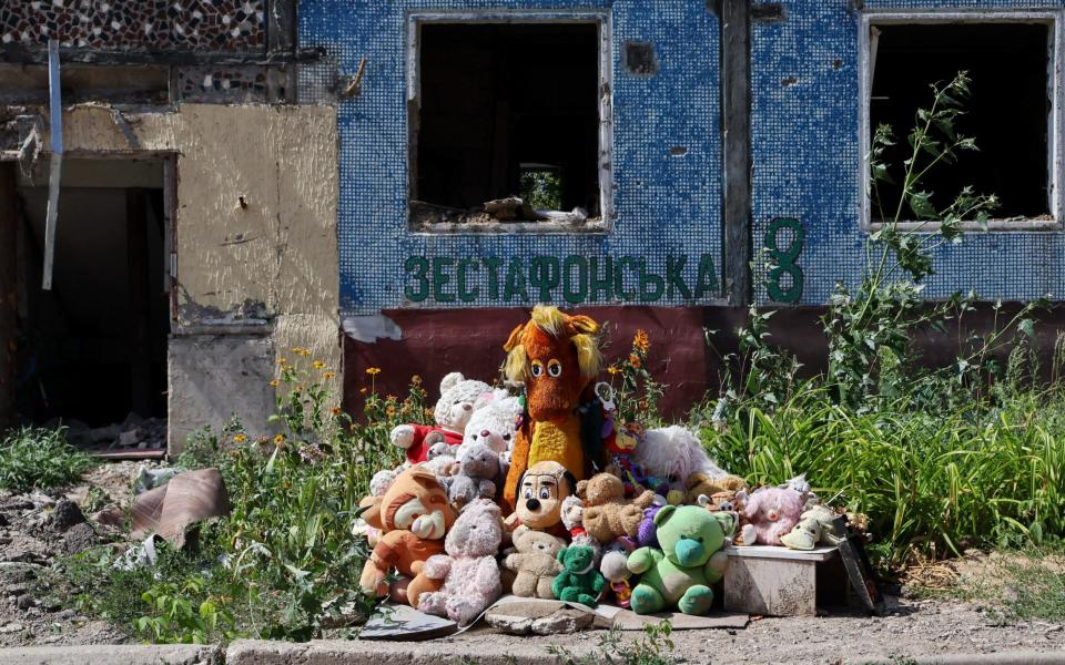 A pile of soft toys in front of a ruined and overgrown building