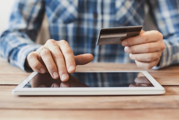 A man scrolling along a digital tablet while holding a credit card in his other hand.