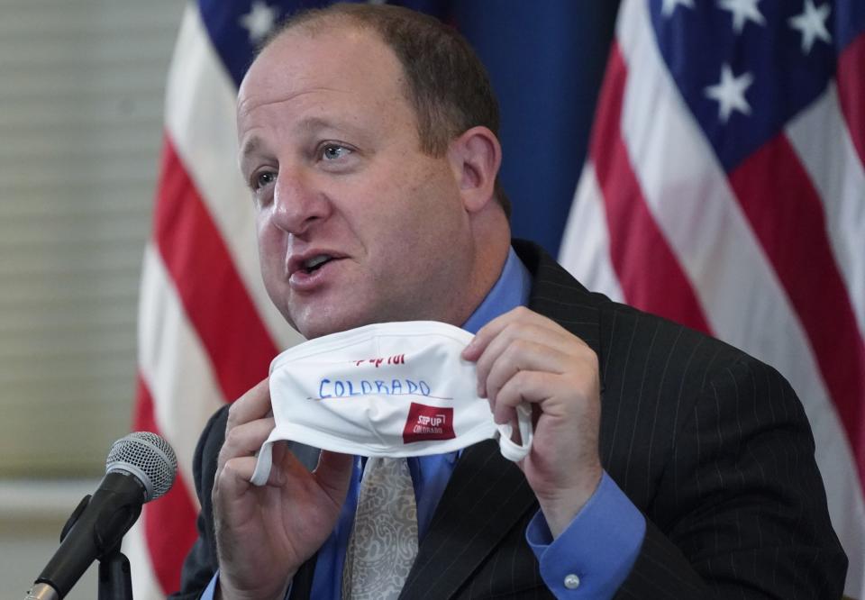 FILE - In this Tuesday, Oct. 20, 2020, file photo, Colorado Gov. Jared Polis holds up a face mask featuring the state's new advertising campaign to encourage residents to protect against COVID-19 during a news conference about the steady increase in cases of the new coronavirus in the state in Denver. Colorado Gov. Polis is quarantining himself after learning that Aurora Mayor Mike Coffman tested positive for the coronavirus. Coffman's diagnosis on Sunday, Oct. 25, 2020, came over a week after he and the governor appeared with other officials at a news conference. A Polis spokesperson said the governor would quarantine while waiting to hear from contact tracers. Coffman said he worked from home starting Thursday after not feeling well and his symptoms were gone by Saturday. He says he got a rapid test Sunday in hopes of being cleared to return to his office and schedule but will now quarantine at home. (AP Photo/David Zalubowski, File)