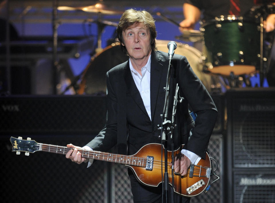 Paul McCartney performs on stage while playing a guitar