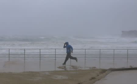 A man runs past heavy seas as sand is blown by heavy winds inland at Sydney's Bondi Beach, April 21, 2015. REUTERS/Jason Reed