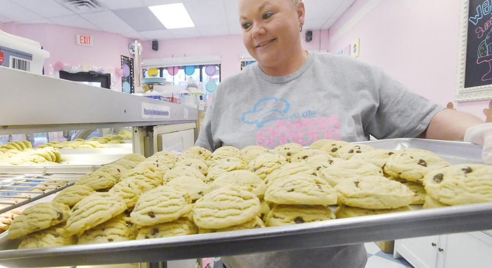 Ye Olde Sweet Shoppe decorator Jessica Francis loads a tray of chocolate-chip cookies into a display case at the downtown Erie cookie and pastry shop.