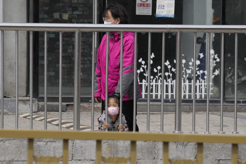 A child wearing a mask looks out from a barrier near closed shops on Monday, May 9, 2022, in Beijing. (AP Photo/Ng Han Guan)