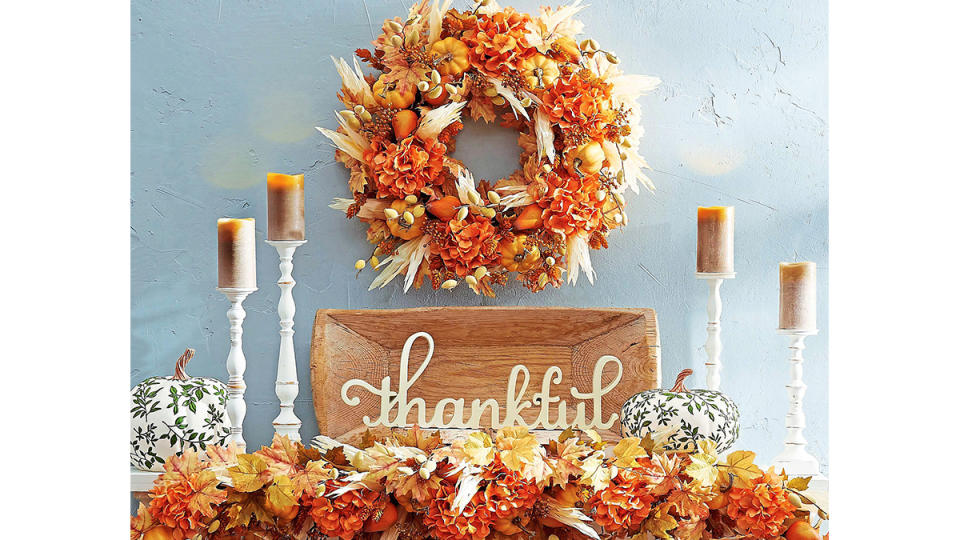 Fall mantel decor ideas: Fireplace mantel or floating shelf decorated cottage style with an orange leafy wreath and garland, white candlesticks, wooden tray and wooden cutout 