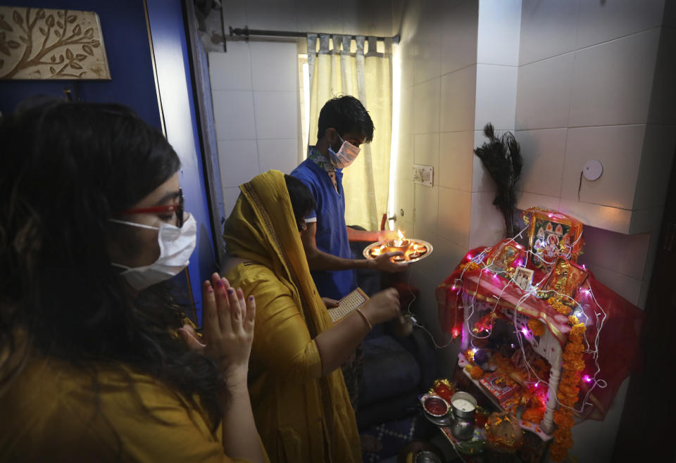 A family, wearing face masks as a precaution from coronavirus, pray inside their house marking the start of Navratri festival, where Hindu fast for nine days, in New Delhi, India, Wednesday, March 25, 2020. (AP Photo/Manish Swarup)