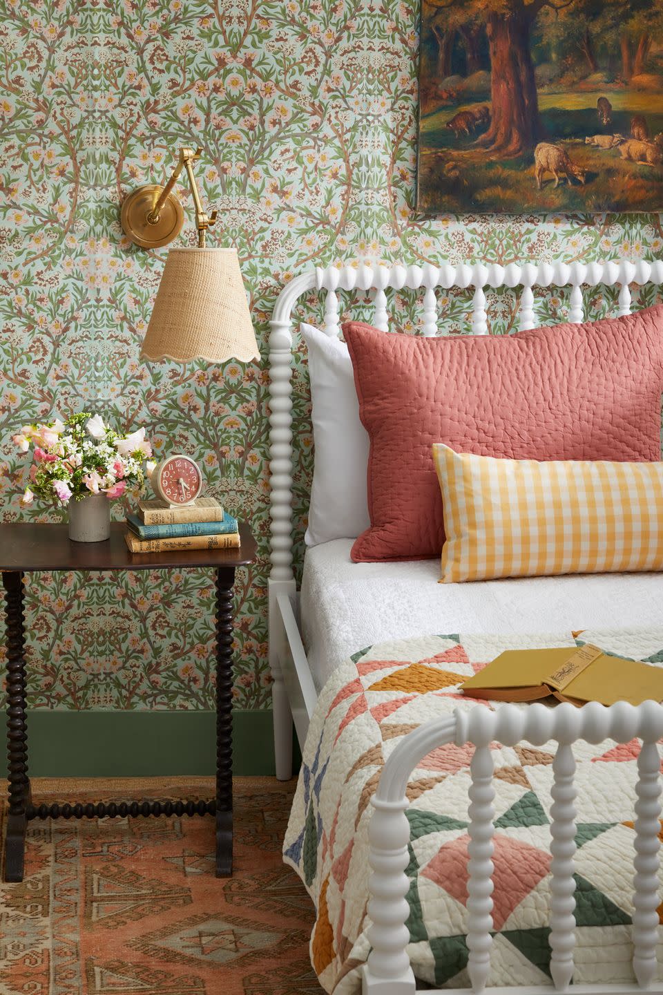 a guest bedroom with floral wallpaper and a white jenny lind bed with coral and yellow pillows and quilt