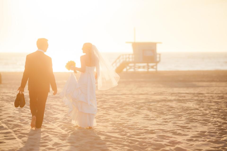 A bride and groom near a lifeguard shack on the beach in Redondo Beach