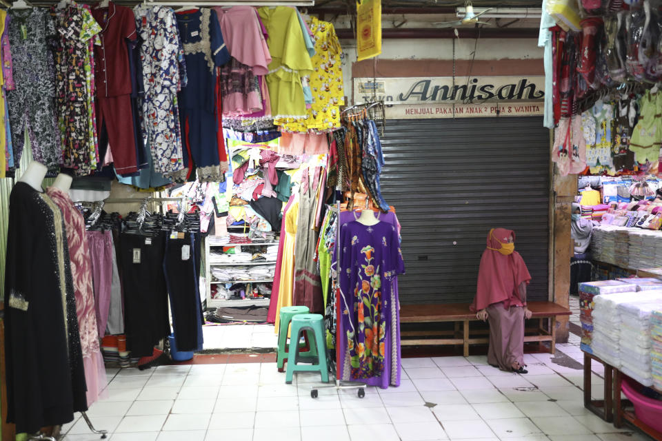 A clothes seller waits for costumers at a quiet market in Jakarta, Indonesia, Friday, April 10, 2020. Authorities began stricter measures to halt the new coronavirus' spread in Indonesia's capital Friday, with its normally congested streets empty after death toll spiked in the past week. (AP Photo/Achmad Ibrahim)