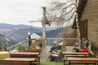Tourists sit on the terrace of a hotel in Vlasic, a ski resort affected by unusual warm weather in Bosnia, Tuesday, Jan. 3, 2023. The exceptional wintertime warmth is affecting ski resorts across Bosnia, prompting tourism authorities in parts of the country to consider declaring a state of natural emergency. (AP Photo/Almir Alic)
