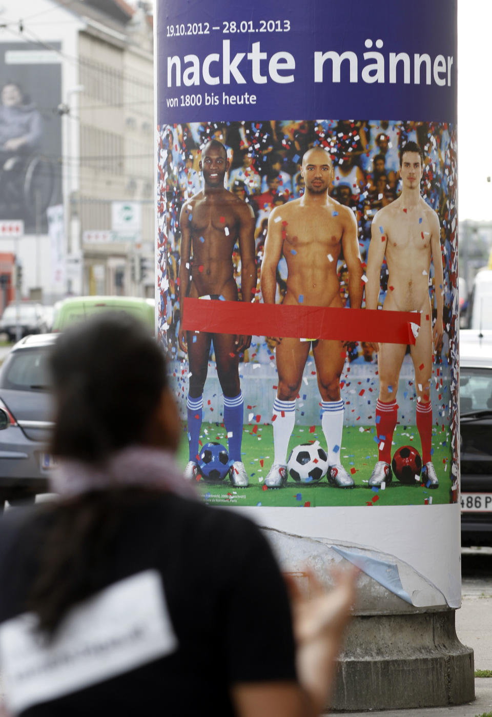 In this picture taken Oct. 18, 2012 a person passes a poster showing three naked men which has had red tape added to cover the sensitive parts of the three men, in Vienna, Austria. Poster reads: "Naked Men". A prestigious Vienna museum, The Leopold Museum, has been forced to cover up a graphic poster advertising a new show devoted to male nudity, after protests that it is offensive. The show — "Nude Men from 1800 to Today" — opened its doors Friday Oct. 20, looking at how artists have dealt with the theme of male nudity over the centuries. (AP Photo/Ronald Zak)