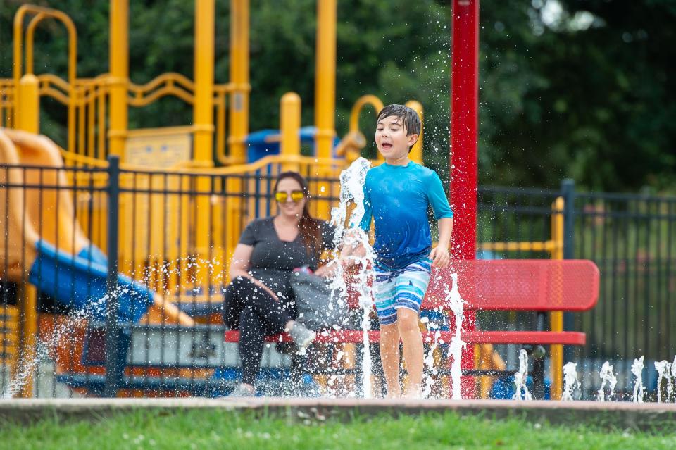 Seven yr old Madden Cashat cooling off at the splash pad at Girard Park as his mother Michelle Champagne watches from a bench. Wednesday, July 31, 2019.