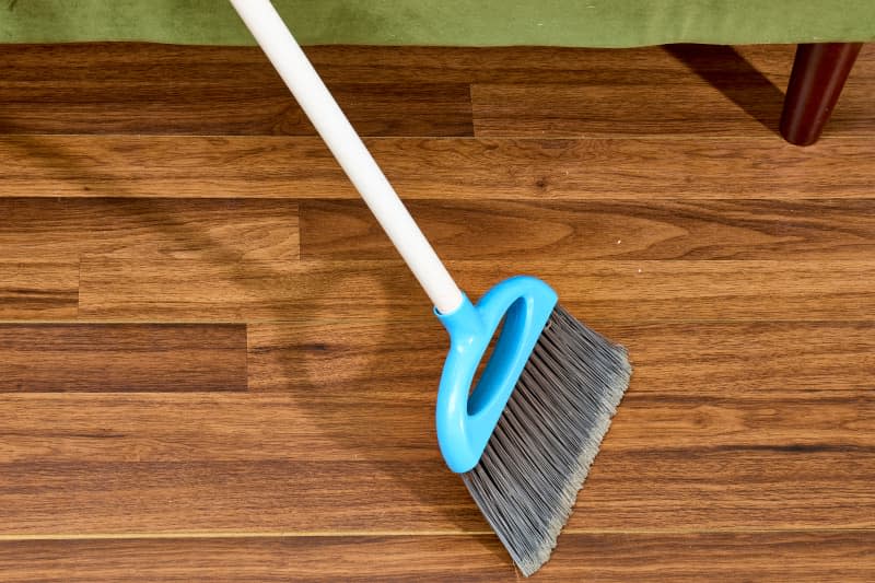 overhead shot of a white and blue broom sweeping up a clean hardwood floor