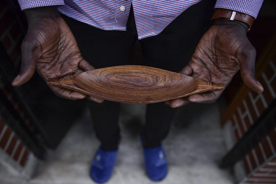 Mbaye Babacar Diouf, 33, holds a small wooden boat as a reminder of the boats migrants travel in, at his home in the basque city of Algorta, northern Spain, Wednesday, Nov. 18, 2020. Mbaye Babacar Diouf's life as a migrant in Europe took a turn for the better when he was adopted in Spain at the age of 28. That enabled him to pay his debts to human traffickers, study nursing and find a job at a Spanish hospital. Now he's giving back to the community. In a Bilbao hospital he cares for COVID-19 patients. (AP Photo/Alvaro Barrientos)