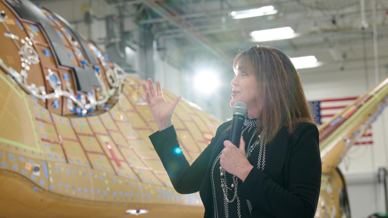  janet kavandi holding a microphone next to sierra space dram chaser under construction. far in the background is a u.s. flag 