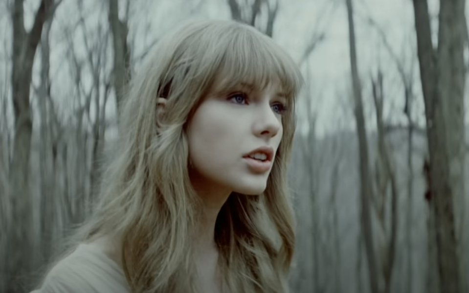 Taylor Swift looking to the side in a natural setting with bare trees